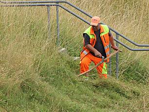 Werkhofmitarbeiter mäht mit Sense